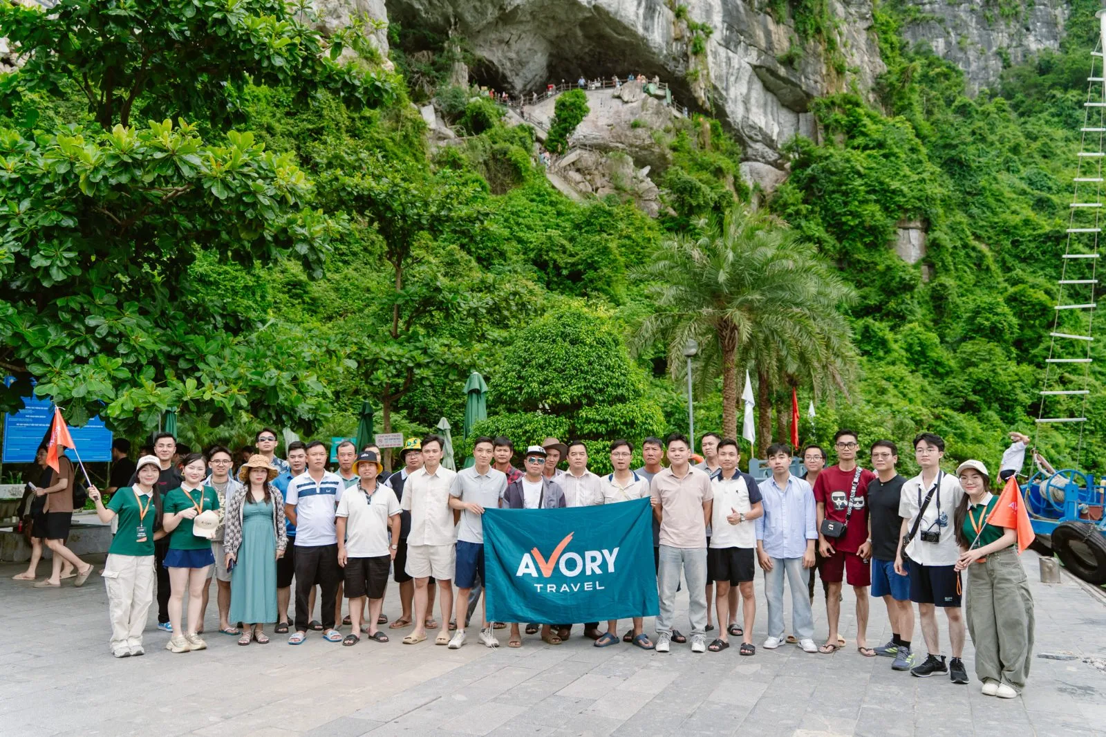 Đoàn khách chụp ảnh cùng cờ Avory Travel trước cửa hang